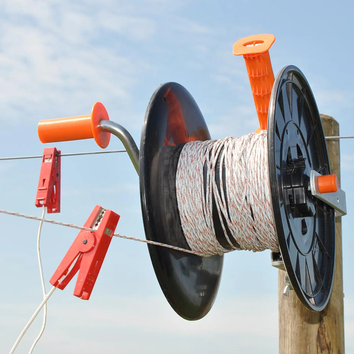 Spool of wire with orange clips against a blue sky
