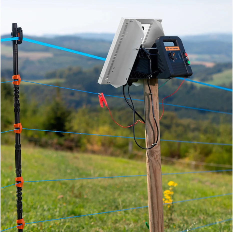 Electric fence control panel on a wooden post with a scenic background of fields and trees.