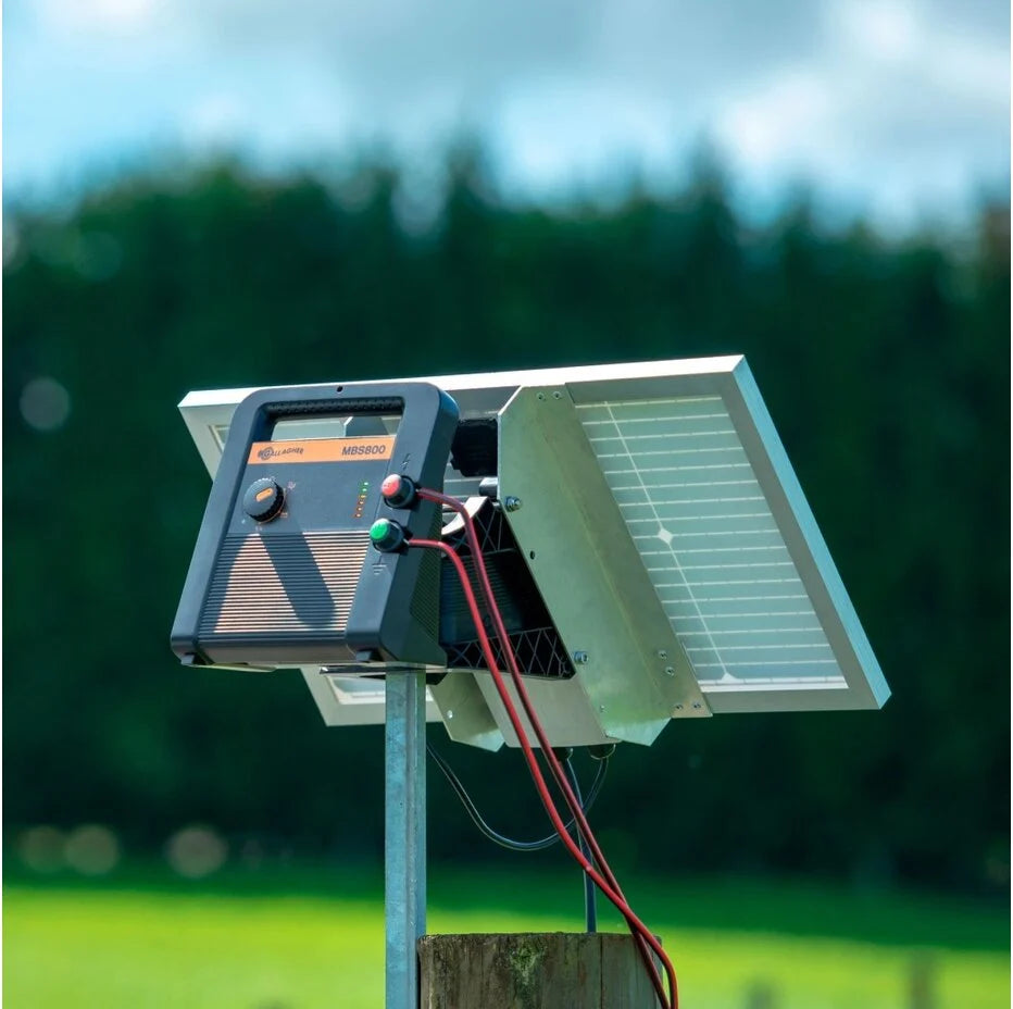 Solar panel and battery system on a post with a blurred green field and blue sky in the background