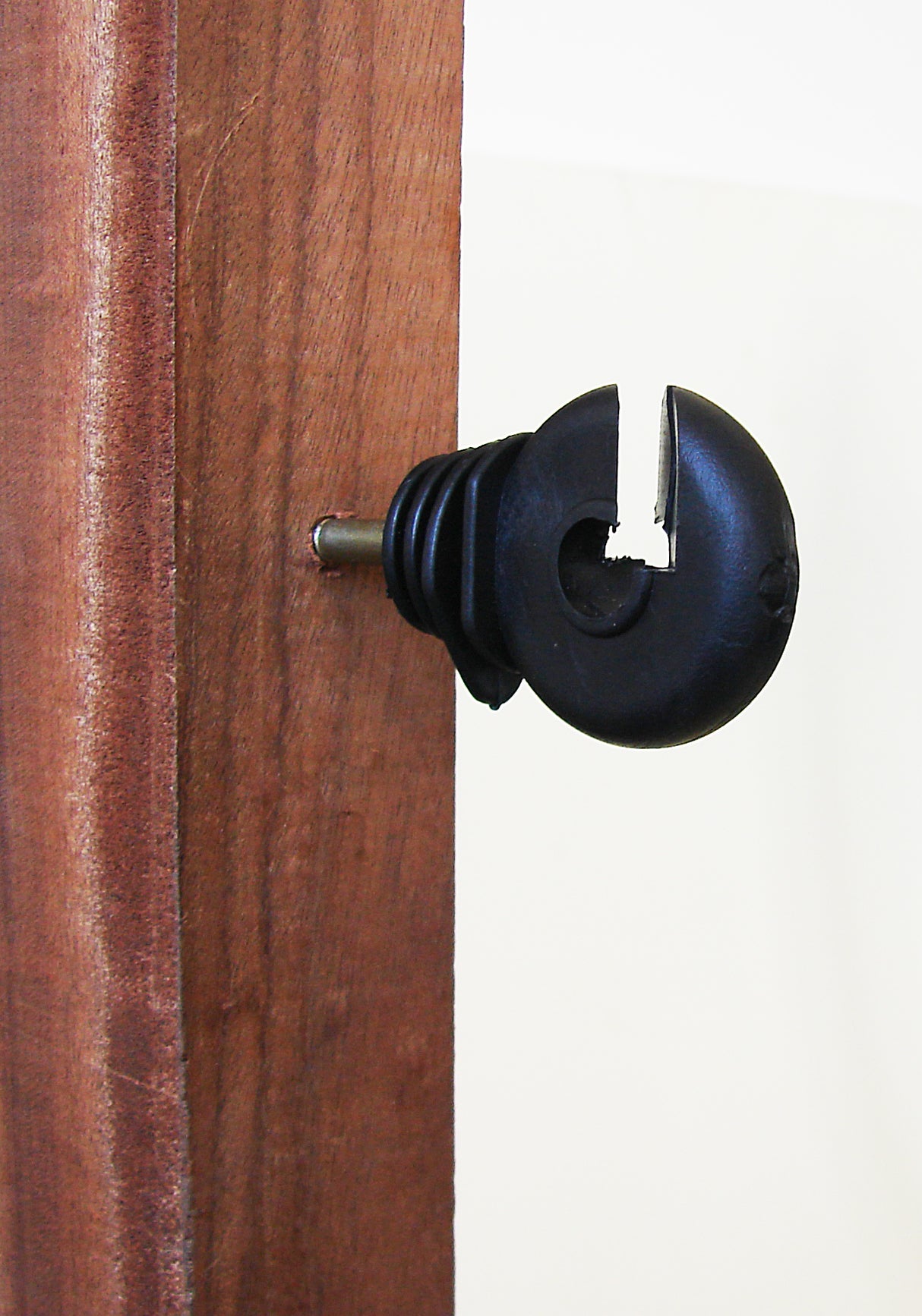 A hotline black screw-in ring insulator for wire and rope, attached to a wooden post.
