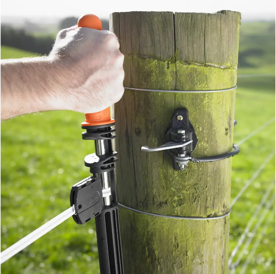 Person using a fence post connector tool on a wooden fence post with a grassy field background.