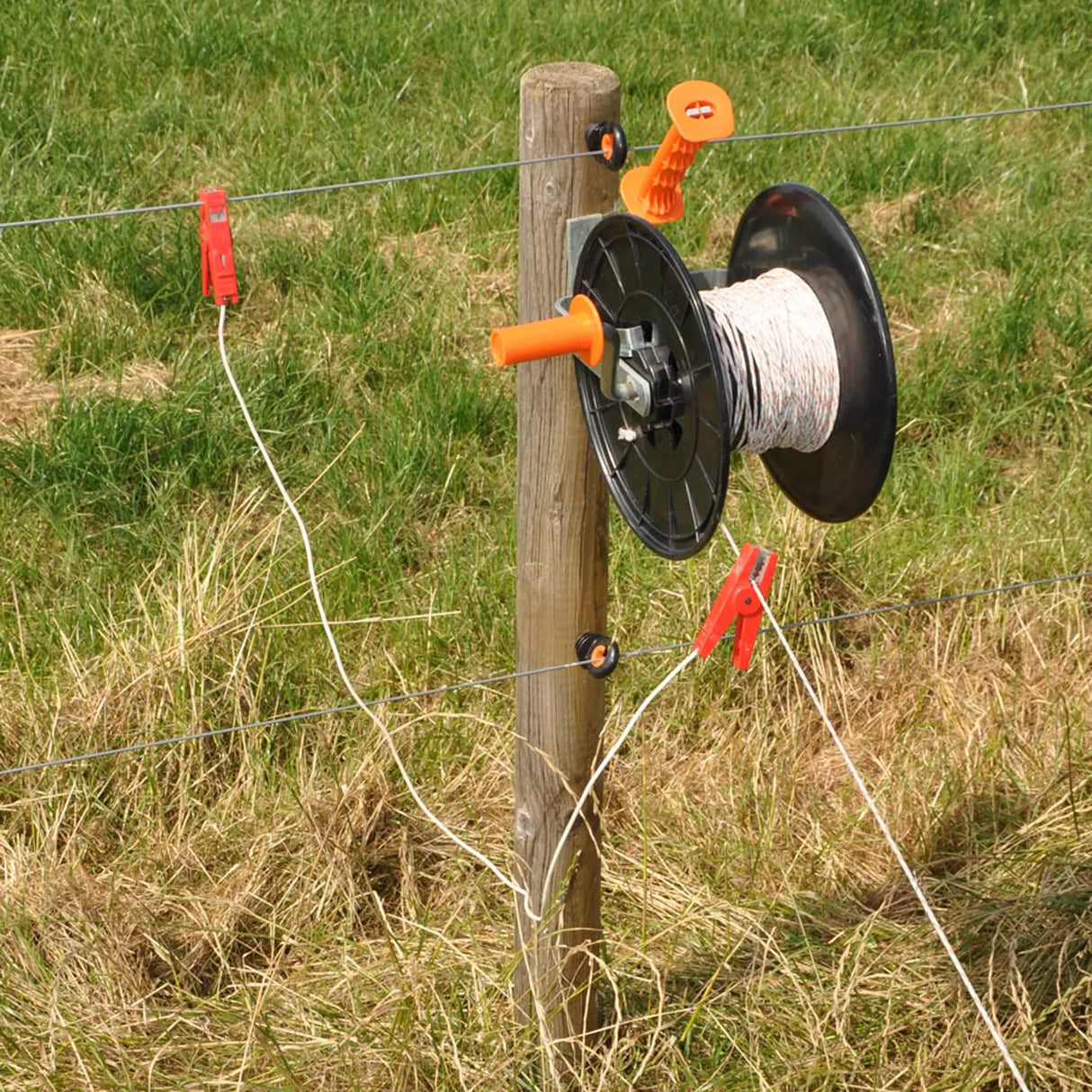 Fence wire reel with clips attached to a wooden post